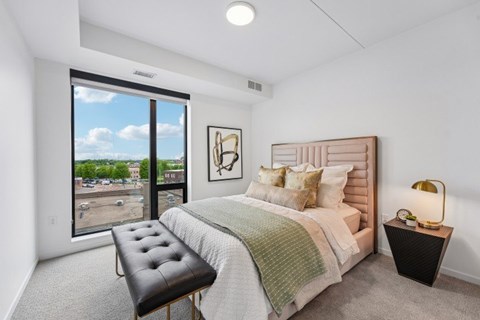 A bedroom with a large bed, a bench, and a window overlooking a parking lot.