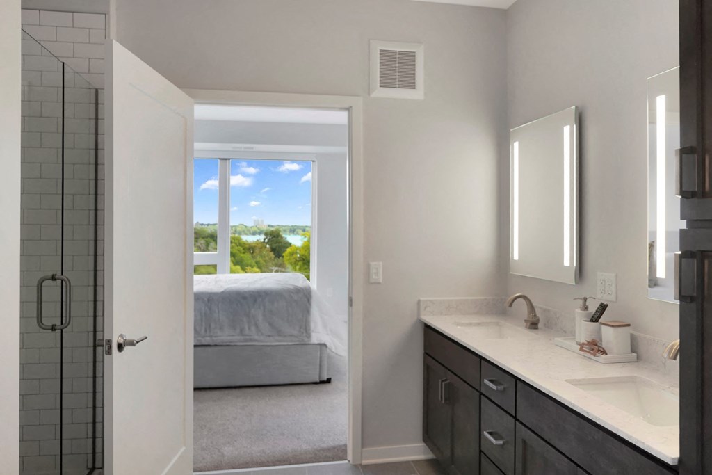 a bathroom with a large window and a bed in the background