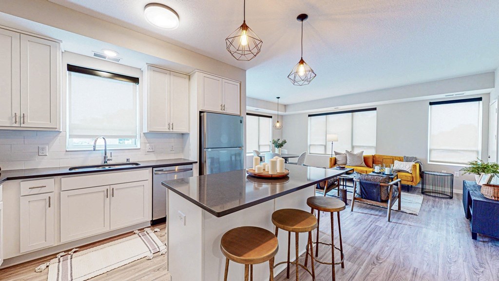 a kitchen and living room with white cabinets and a large island with stools at The Morrison, Rosemount Minnesota