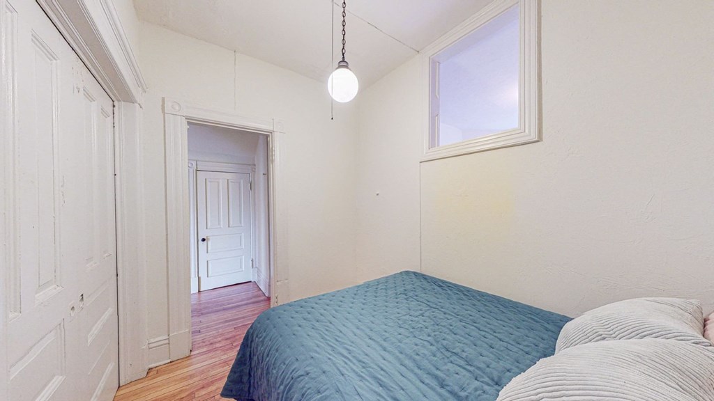 A bedroom with a blue bedspread and a window.
