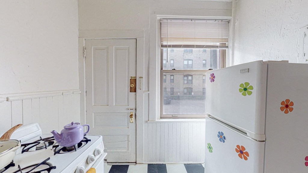 A white fridge with flower decals sits in a kitchen next to a stove.