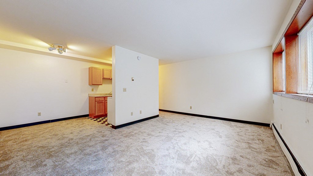 a bedroom with a white wall and a white door with a kitchen in the background