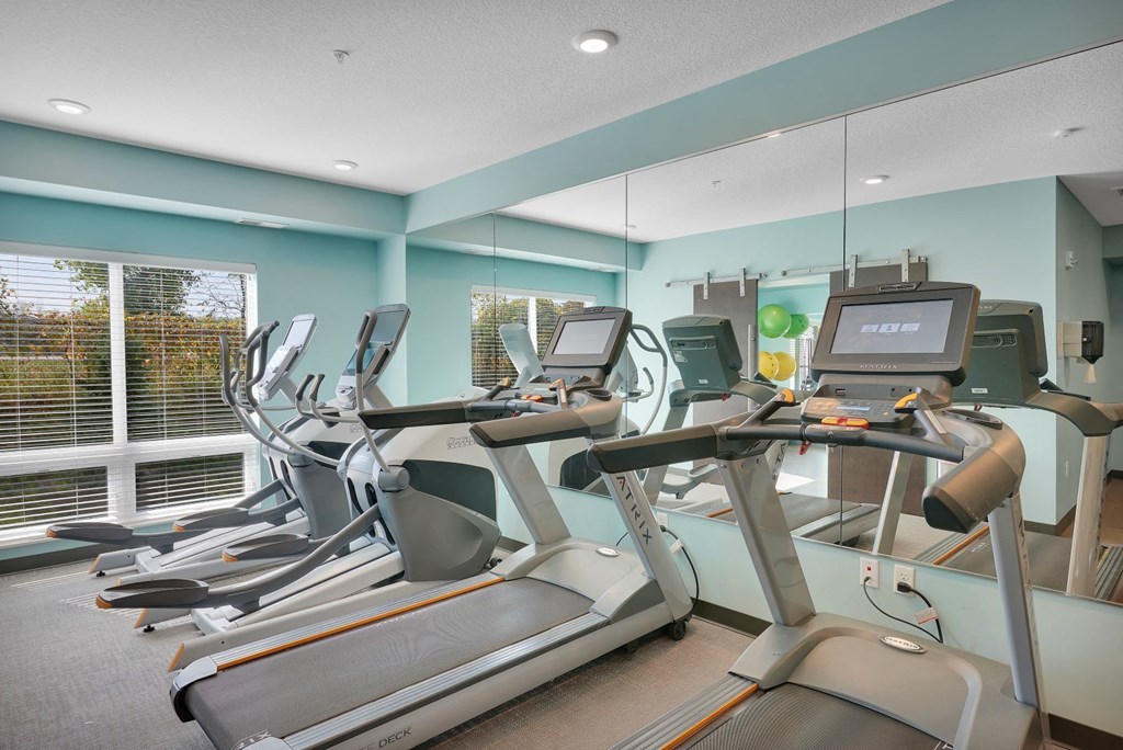 a gym with cardio machines and a large window
