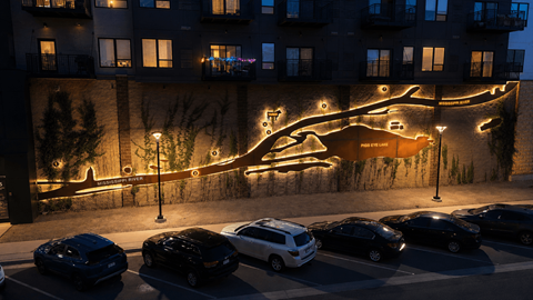 A building with a tree-like mural on its side is lit up at night.
