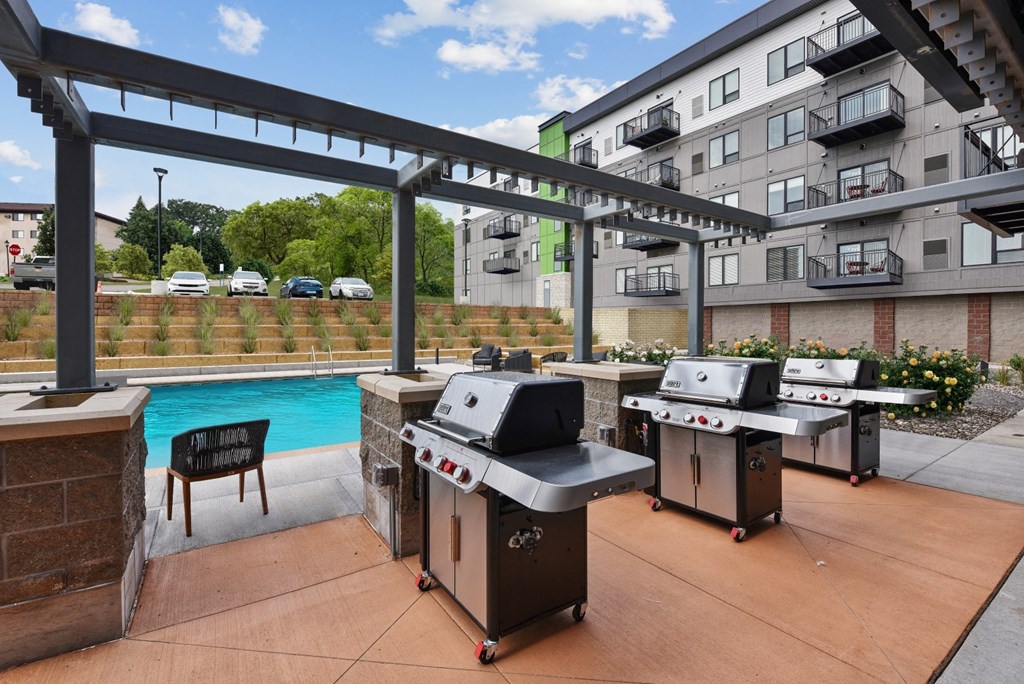two barbecue grills sit on a patio next to a pool with an apartment building in the