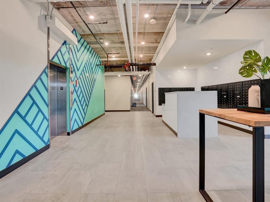 A long hallway with a blue and green patterned wall on the left and a wooden table on the right.