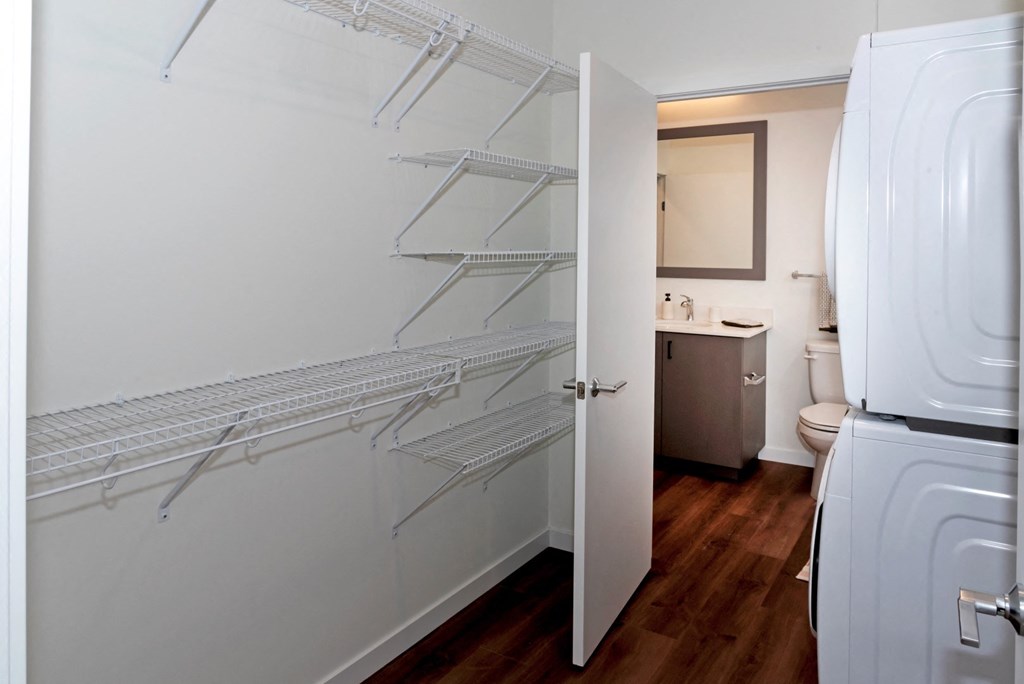 a bathroom with white fixtures and white walls and a closet with shelves and a toilet