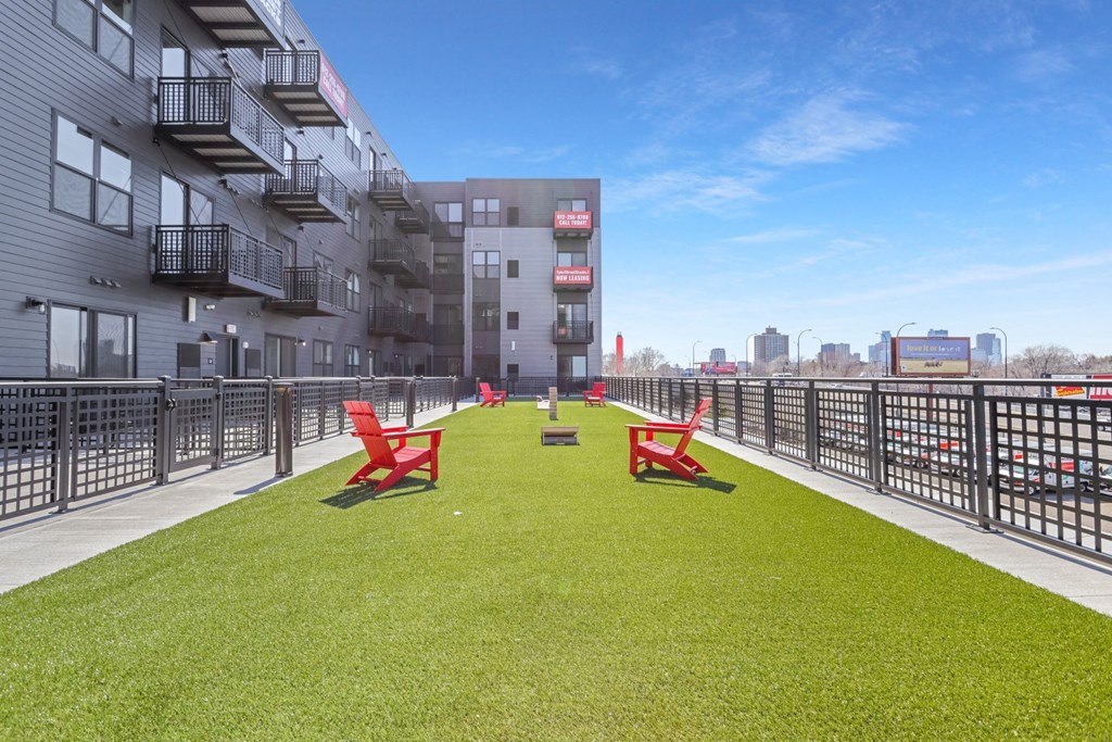 a grassy area with red chairs on a balcony of an apartment building