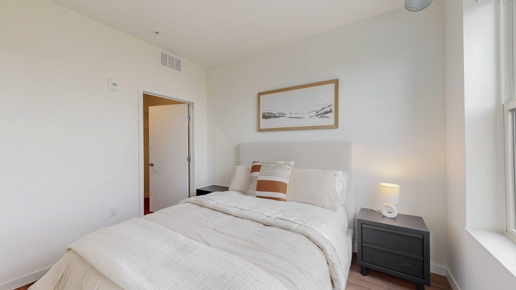 A bedroom with a large bed, nightstand, and a picture on the wall.