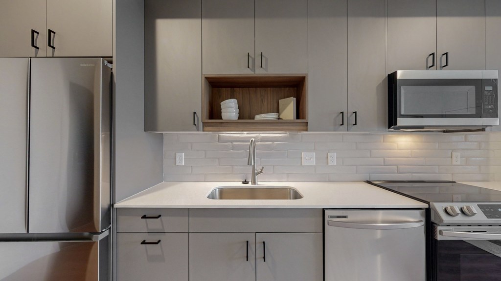A modern kitchen with a stainless steel refrigerator, a white sink, and a microwave above the stove.