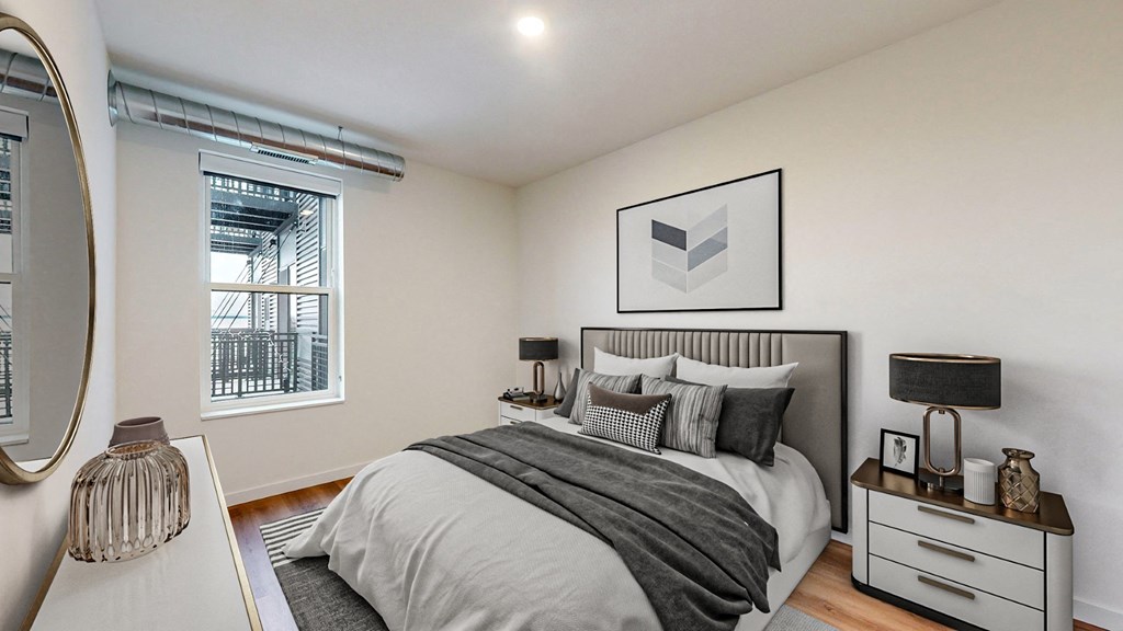 A bedroom with a large bed, a nightstand with a lamp, and a mirror on the wall.