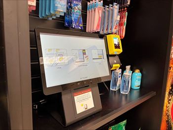 A computer monitor with a screen showing a graphic of a hand holding a credit card and a barcode scanner is on a shelf with various products.