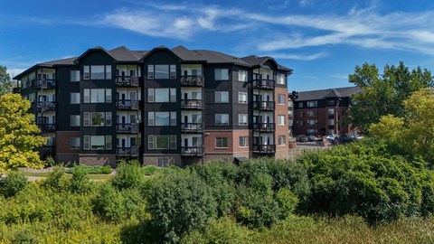 A large apartment building with balconies and multiple windows is surrounded by greenery.