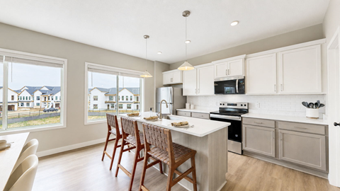 A kitchen with white cabinets and a large island with chairs around it.