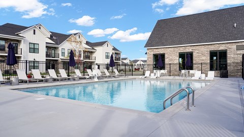 A swimming pool surrounded by lounge chairs and umbrellas in front of a building.