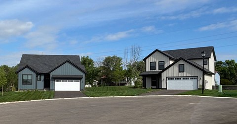 Two houses with garages are situated on a paved lot.