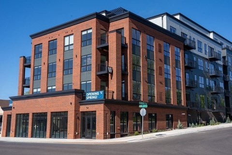 A red brick building with a blue sign that says "OPENING SPRING" on the front.