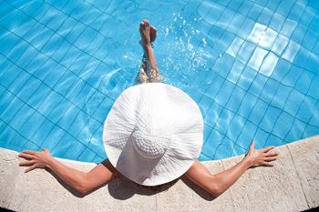 a woman in a sun hat diving into a swimming pool