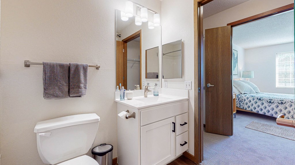 a bathroom with a toilet sink and mirror and a bedroom with a bed