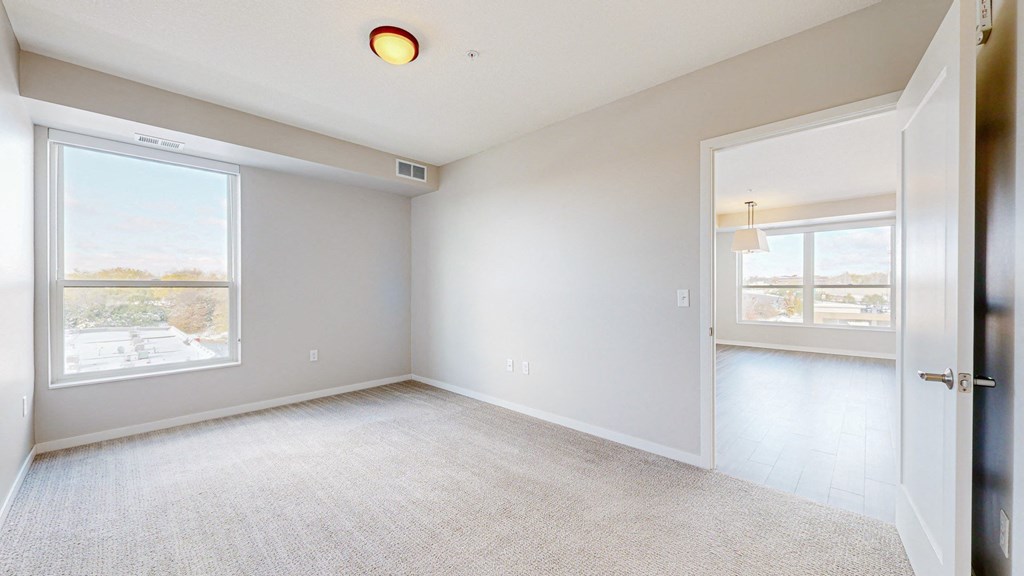 A spacious, empty room with a large window and a door leading to another room.