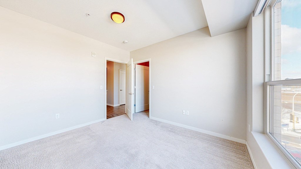 A large, empty room with a carpeted floor and a window on the right side.