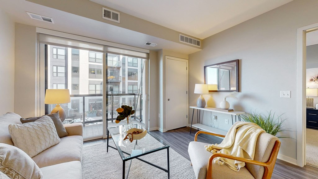 A living room with a white sofa, a glass coffee table, and a large window.
