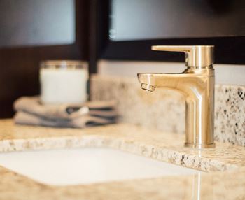 A bathroom sink with a gold faucet and a white candle on the counter.at The Edison at Avonlea, Lakeville Minnesota
