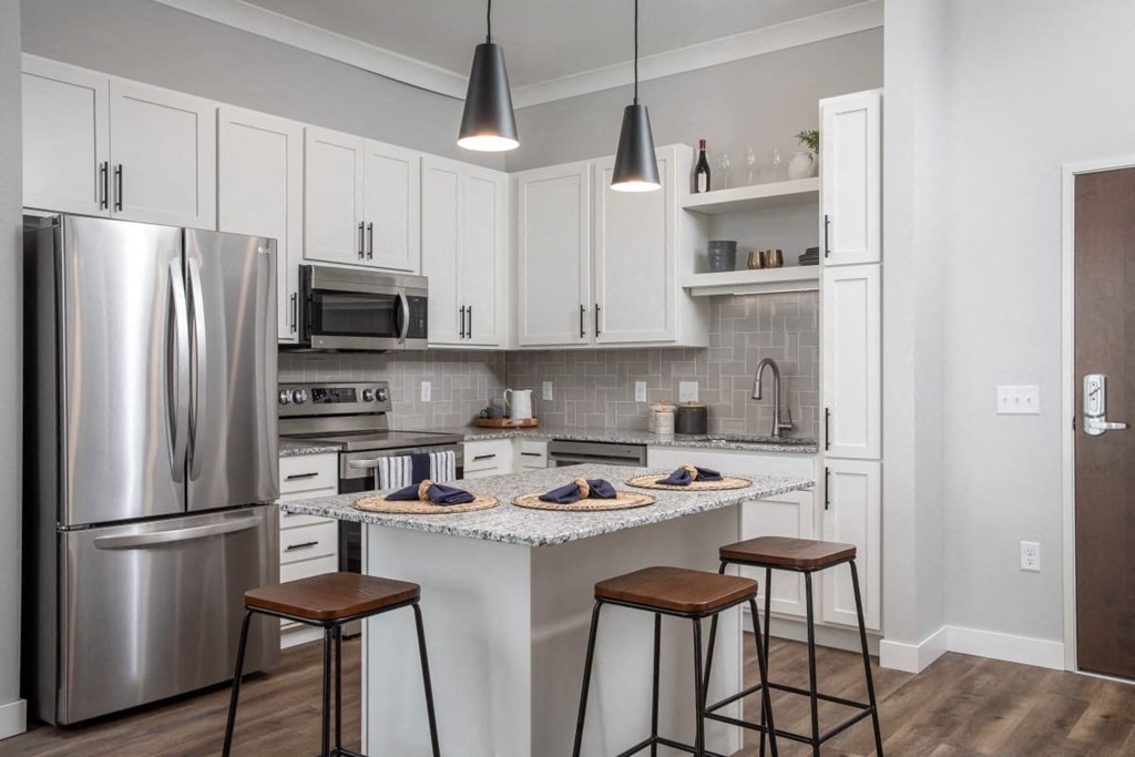 A kitchen with a refrigerator, microwave, oven, and bar stools.at The Edison at Maple Grove, Maple Grove, MN 55311