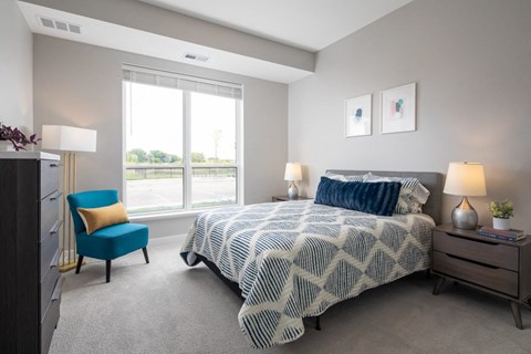 A bedroom with a large bed and a blue chair.at The Edison at Maple Grove, Maple Grove, MN