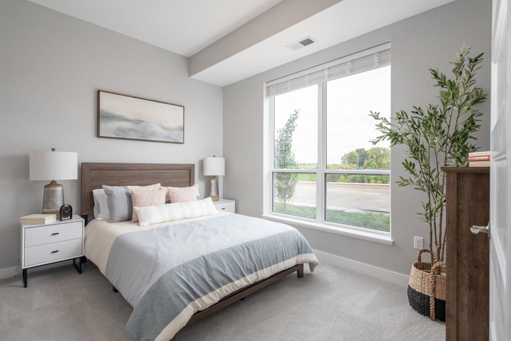 A bedroom with a large bed, two lamps, and a painting on the wall.at The Edison at Maple Grove, Maple Grove