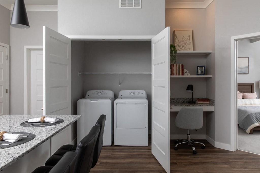 A laundry room with a washer and dryer is open to a bedroom.at The Edison at Maple Grove, Minnesota