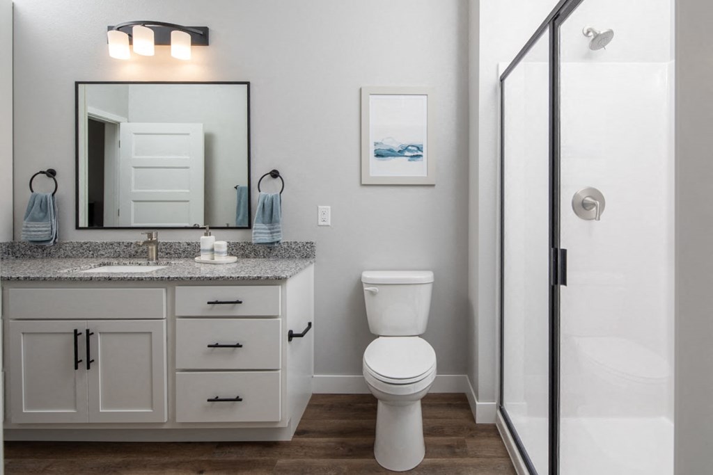 A white toilet sits in a bathroom next to a sink and mirror.at The Edison at Maple Grove, Maple Grove