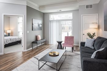 A modern living room with a grey couch, a pink chair, and a coffee table.at The Edison at Maple Grove, Maple Grove