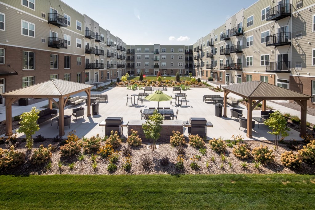 A courtyard with a grassy area, benches, and trees surrounded by apartment buildings at The Edison at Rice Creek I and II, Shoreview, MN 55126