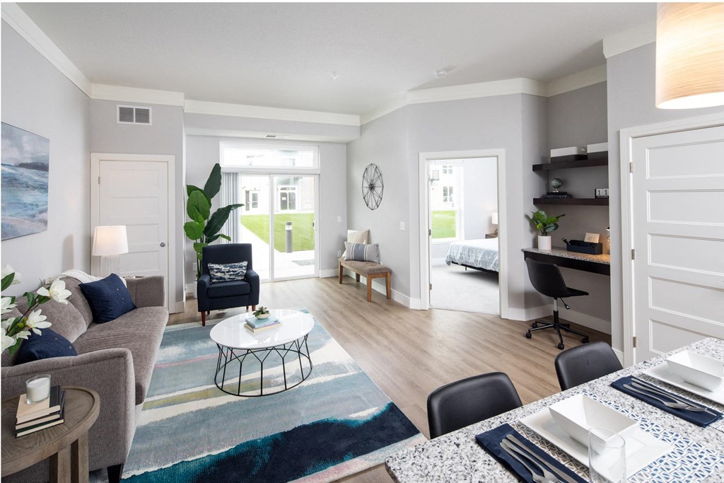 A modern living room with a grey sofa, a coffee table, and a dining table set for two at The Edison at Spirit, Lakeville, 55044