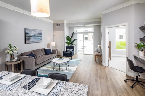 A modern living room with a grey sofa, a coffee table, and a dining table set for two.
