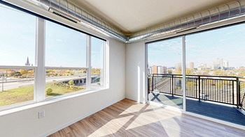 A room with a large window overlooking a cityscape at The Bessemer at Seward Commons Apartments, Minnesota
