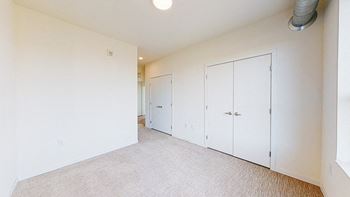 A room with white walls and a carpeted floor with three white doors at The Bessemer at Seward Commons Apartments, Minneapolis, 55404