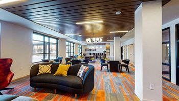 A large room with a long couch and a red chair at The Bessemer at Seward Commons Apartments, Minneapolis, Minnesota