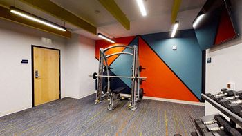 A gym room with a treadmill, weights and a wall with a blue and orange design at The Bessemer at Seward Commons Apartments, Minneapolis, MN,  55404