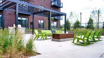 A patio with green chairs and a bench in front of a building at The Bessemer at Seward Commons Apartments, Minneapolis, Minnesota