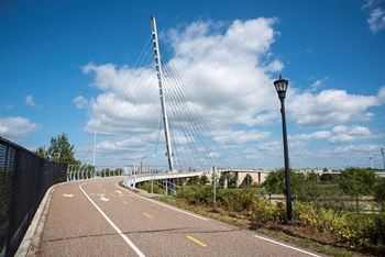 A pedestrian pathway with a lamp post and a bridge in the background at The Bessemer at Seward Commons Apartments, Minneapolis, 55404