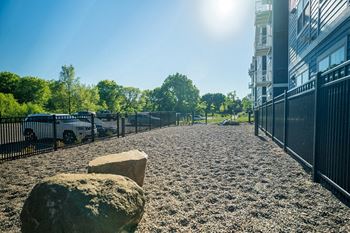 A sunny day in a park with a gravel path, trees, and a fence at The Barnum Apartments, MN, 55110