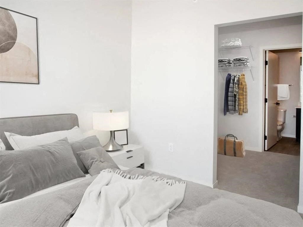 A bedroom with a bed, nightstand, and a closet with clothes.