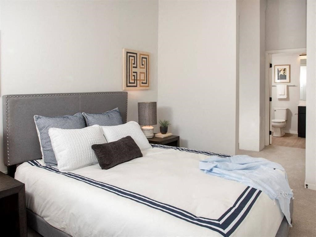 A bed with a white comforter and a blue striped border is in the foreground of a room.