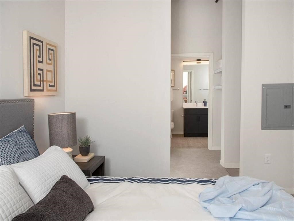 A bedroom with a bed, nightstand, and a mirror in the hallway.