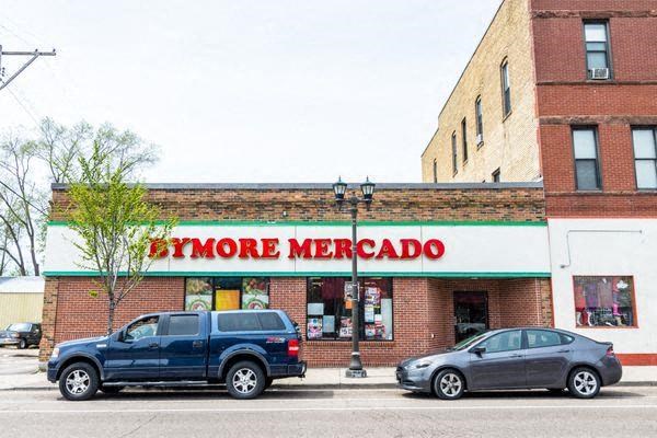 A blue car is parked in front of a store called Bymore Mercado.