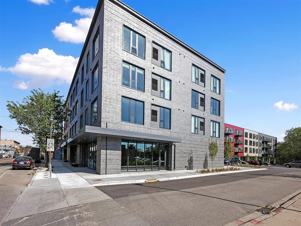 A modern building with a grey facade and large windows is situated on a street corner.