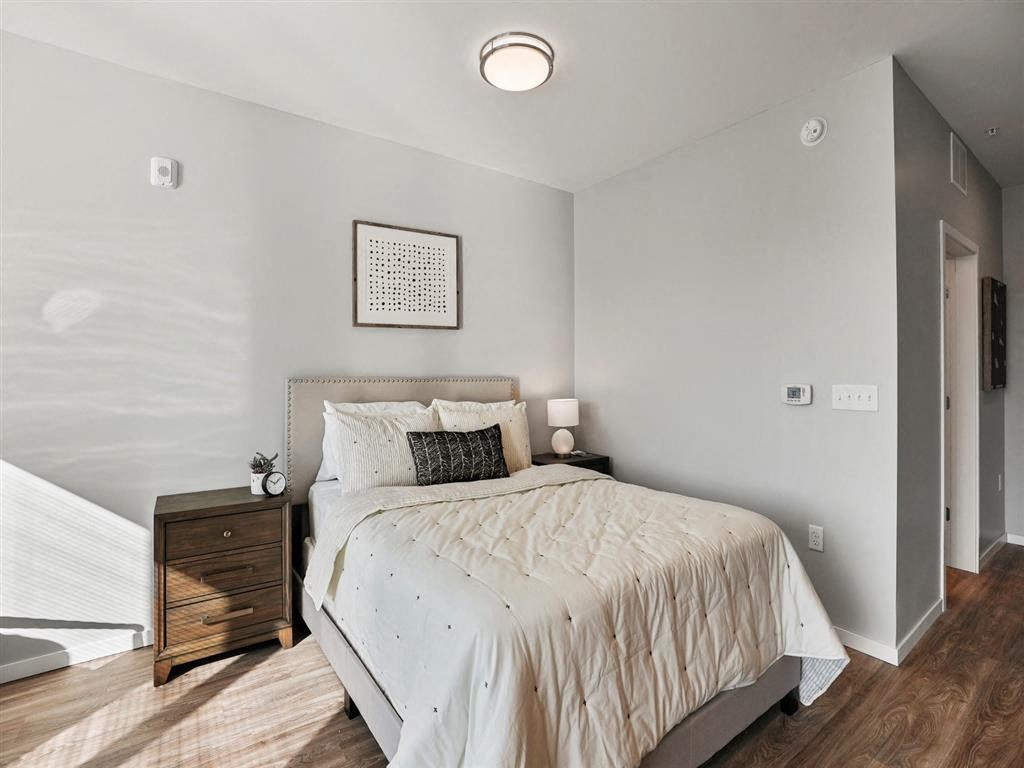 A bedroom with a bed, nightstand, and a window with blinds.