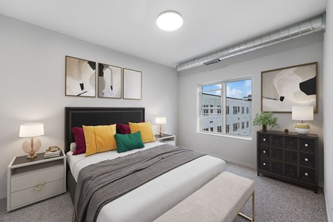 A bedroom with a bed, nightstand, and a window with a view of a building at Soul Apartments, Minnesota 55107